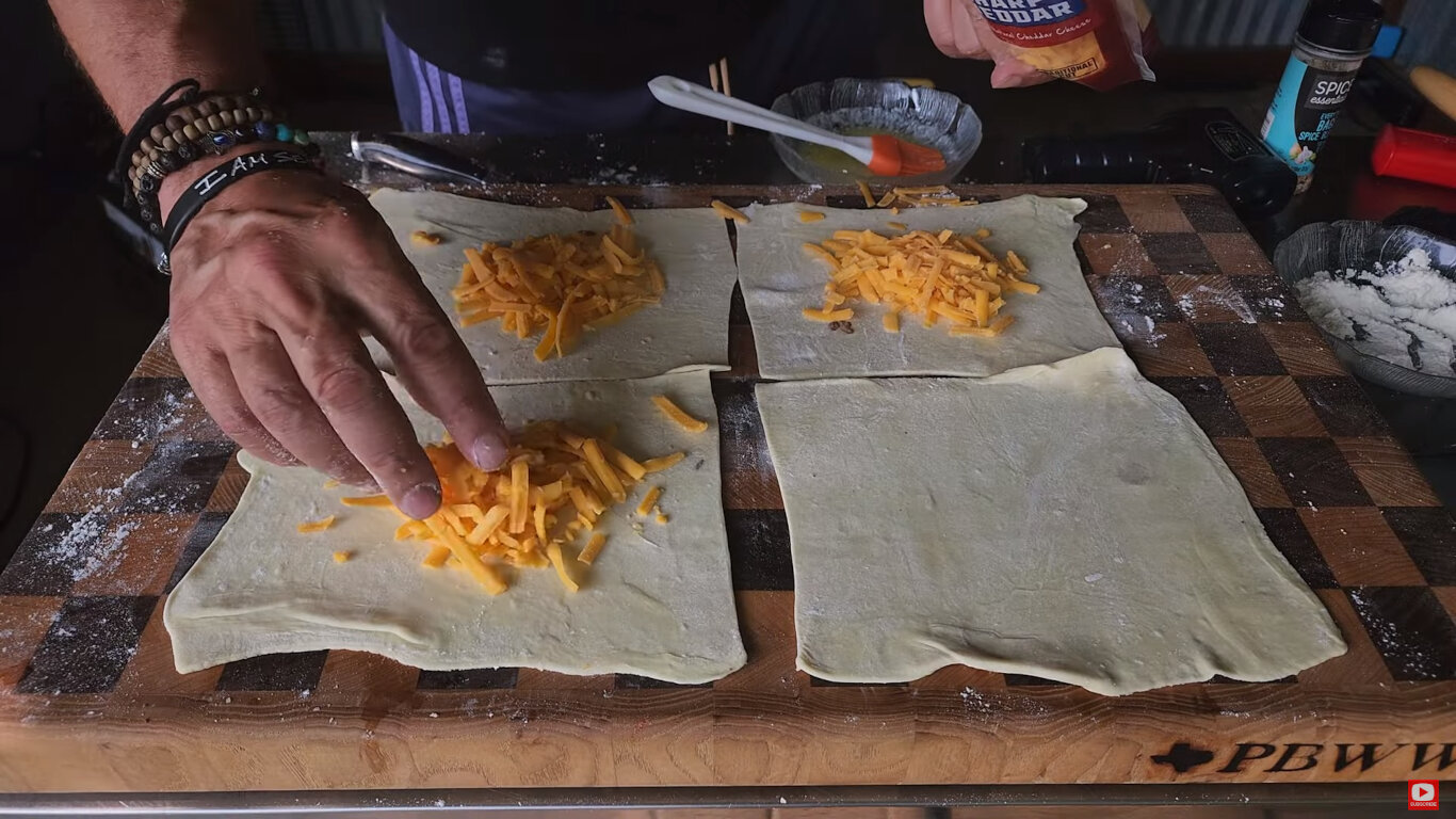 Shredded cheese being added to puff pastry squares